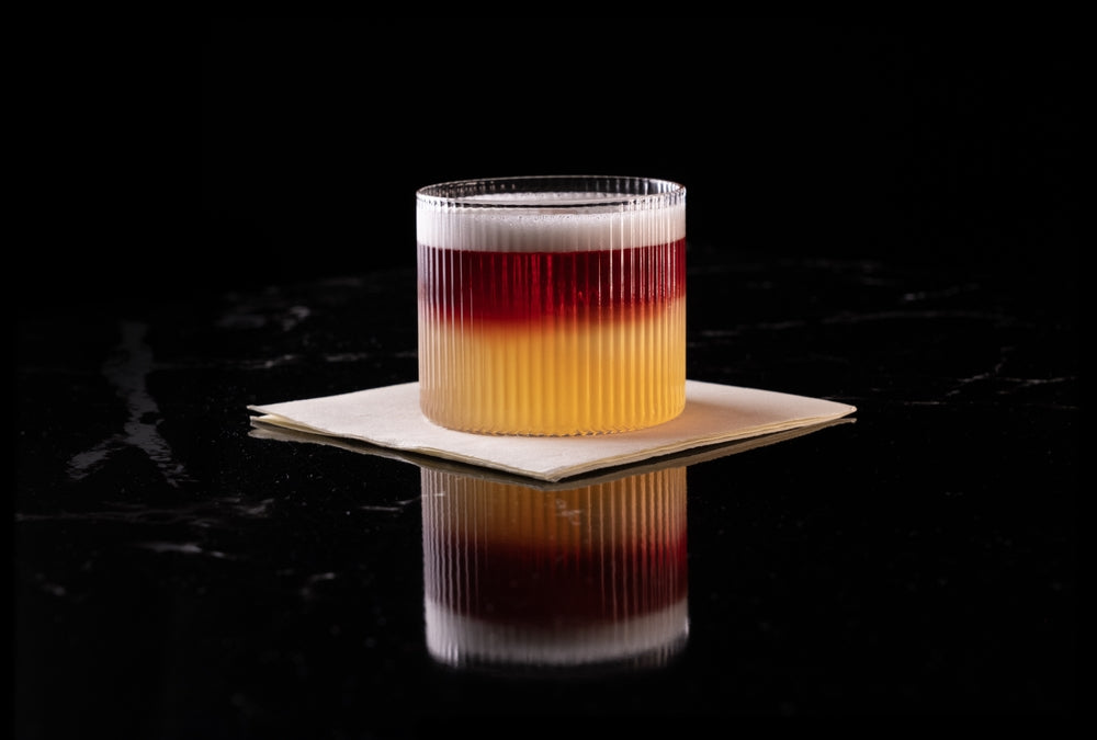 Layered whiskey cocktail using red wine float with vibrant gradient tones served on a sleek black marble surface at Friarwood.