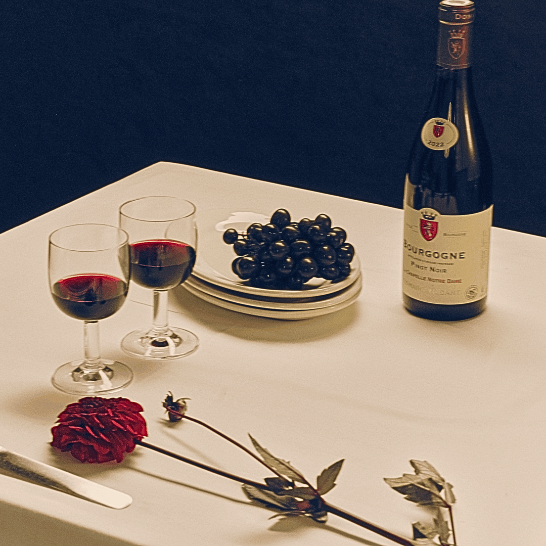 Table setting featuring a bottle of Bourgogne Pinot Noir 2022, two glasses of red wine, fresh grapes, and a red rose, creating a romantic atmosphere.