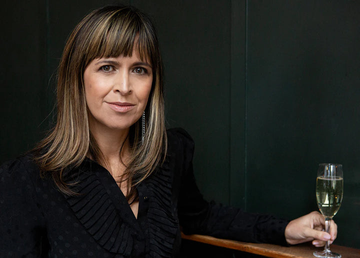 Amanda Thomson, founder of Thomson & Scott, holding a glass of sparkling wine, sitting in an elegant setting.