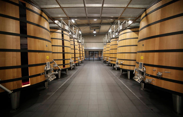 Interior of the winery cellar at Château Dauzac in Margaux, Bordeaux, featuring large oak barrels used for aging wine.