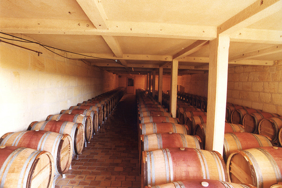 Interior view of Château Figeac's barrel room, showcasing neatly arranged wooden barrels aging fine wine in a traditional stone cellar.