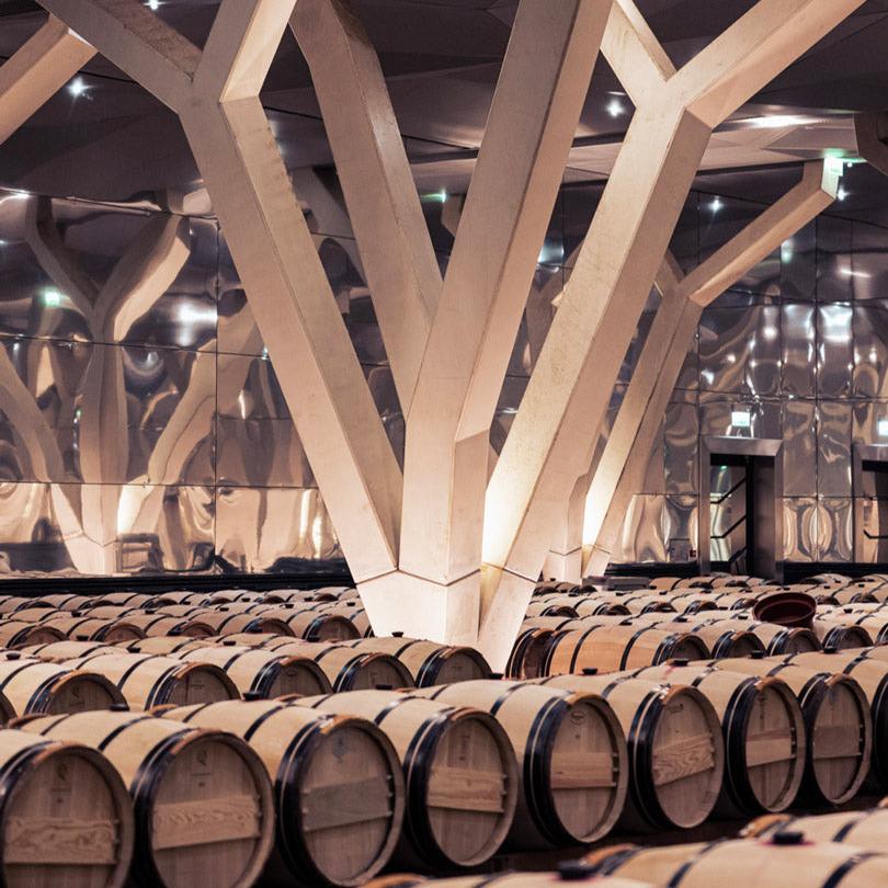 Rows of wine barrels in the Château Talbot cellar with large, geometric white pillars supporting the ceiling.