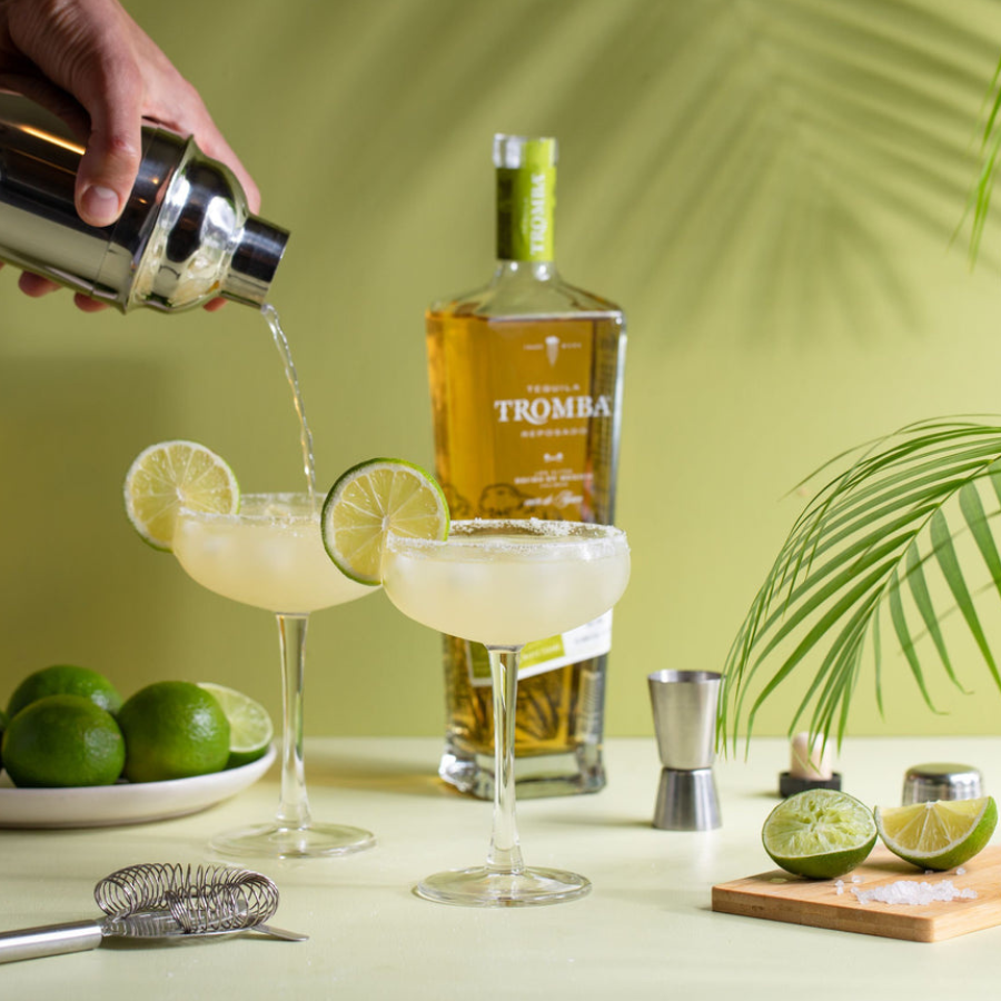 Tromba Reposado Tequila bottle next to margarita glasses and fresh limes on a summer-inspired table setting.