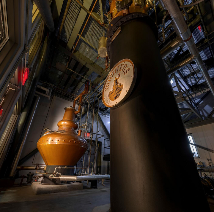 A dramatic angle of Michter's Distillery featuring a copper pot still and large black column still with the Michter's logo displayed prominently.