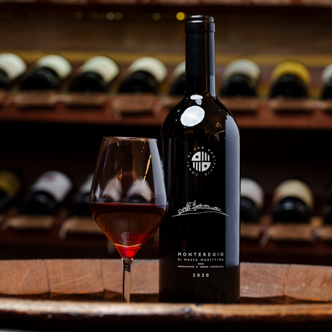 A bottle of Monteregio di Massa Marittima 2020 wine elegantly displayed alongside a filled glass, set against a refined wine cellar backdrop with rows of wine bottles softly lit in the background.