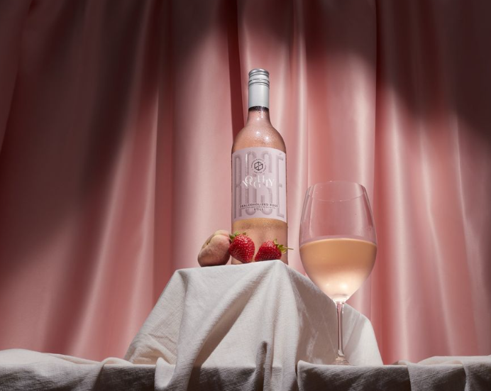 Noughty Still Rosé styled with strawberries and lychee, set against a soft pink background, evoking elegance and indulgence.