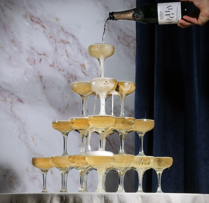 Champagne tower being poured with Noughty Sparkling Chardonnay, creating a cascade of sparkling bubbles.