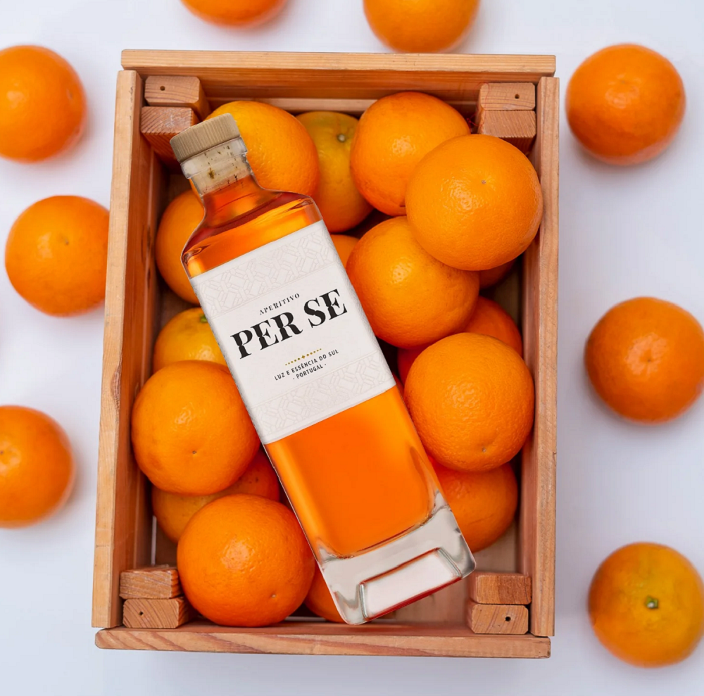 Bottle of Per Se Aperitivo displayed in a wooden crate surrounded by fresh oranges.