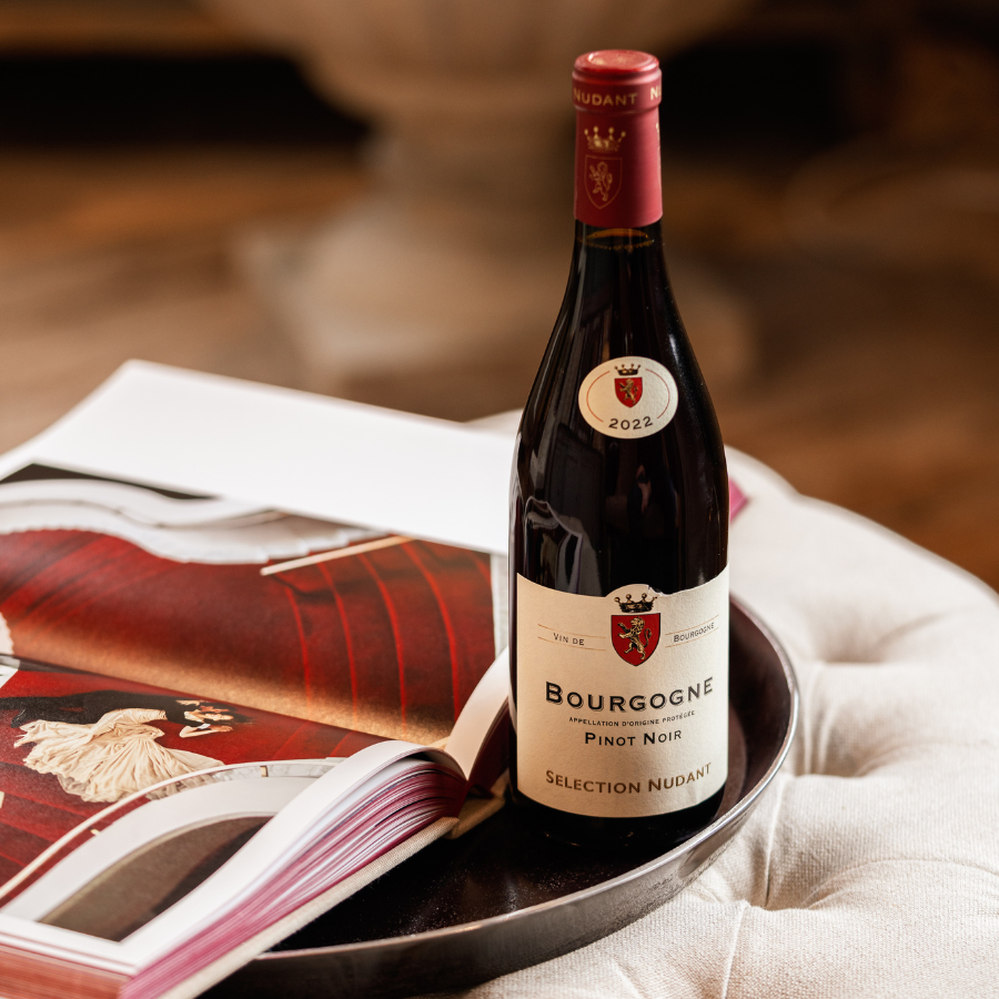 A bottle of Bourgogne Pinot Noir Selection Nudant 2022 displayed on a tray with an open coffee table book, creating a refined wine tasting ambiance.