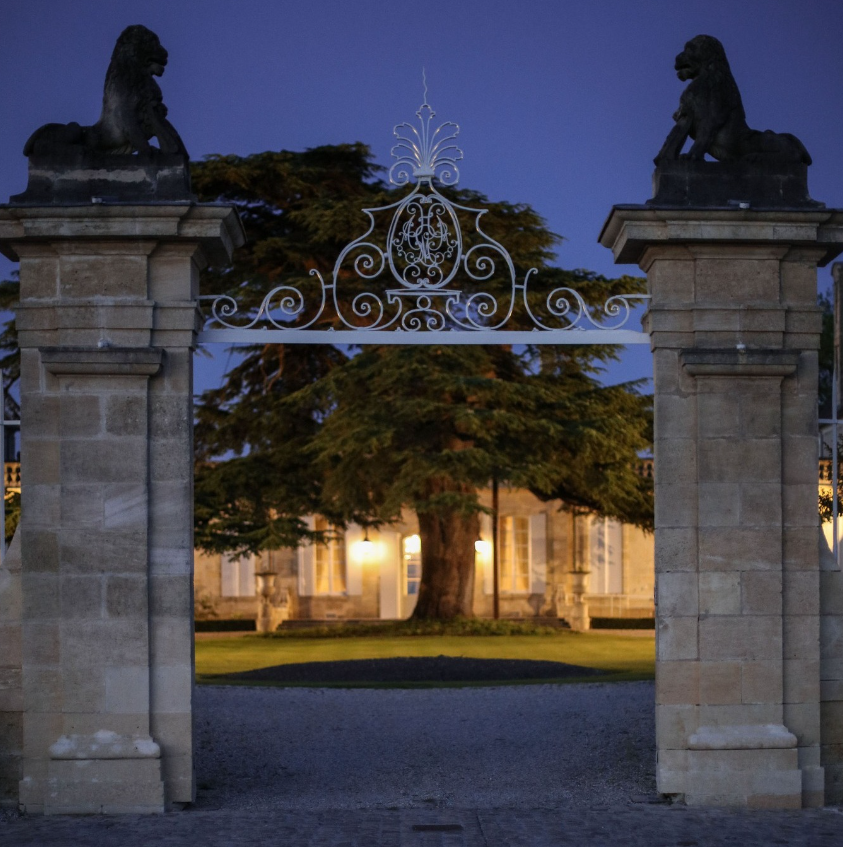 Chateau Beychevelle Ornate gate with lion statues framing the entrance to a chateau at dusk.