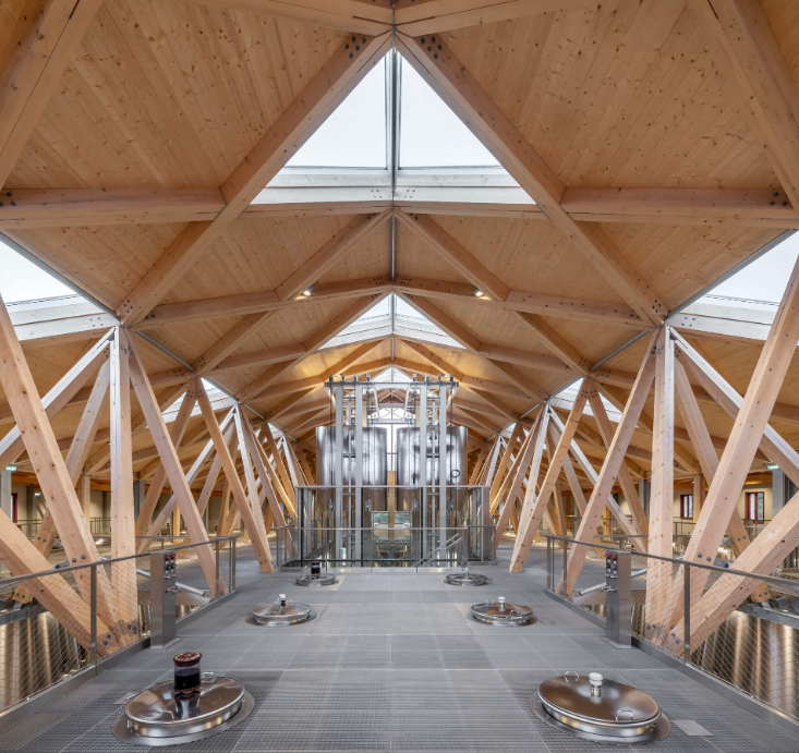 Modern wooden-beamed interior of Château Cantenac Brown winery, featuring stainless steel fermentation tanks and skylights.