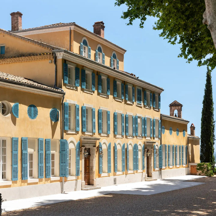 Château d'Esclans estate showcasing its classic Provençal architecture with yellow walls, blue shutters, and surrounding greenery.