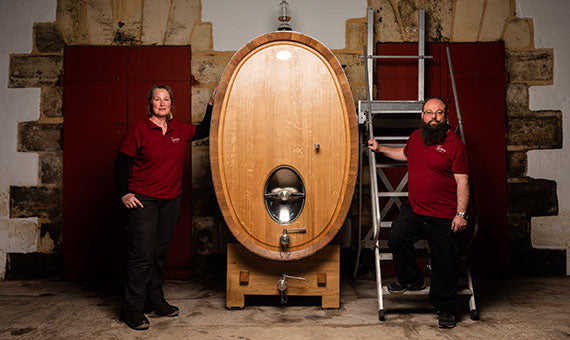 Château Giscours cellar workers standing beside an impressive wooden wine fermentation barrel, showcasing the craftsmanship and dedication involved in producing Bordeaux Grand Cru wines at the Margaux estate.