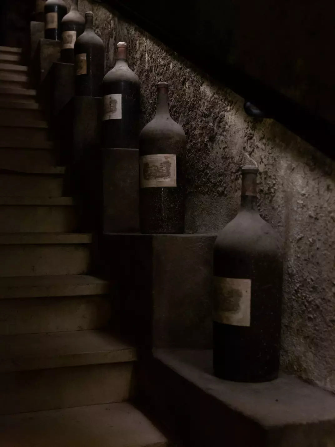 Dust-covered aged wine bottles from Château Lafite Rothschild resting on a historic staircase.