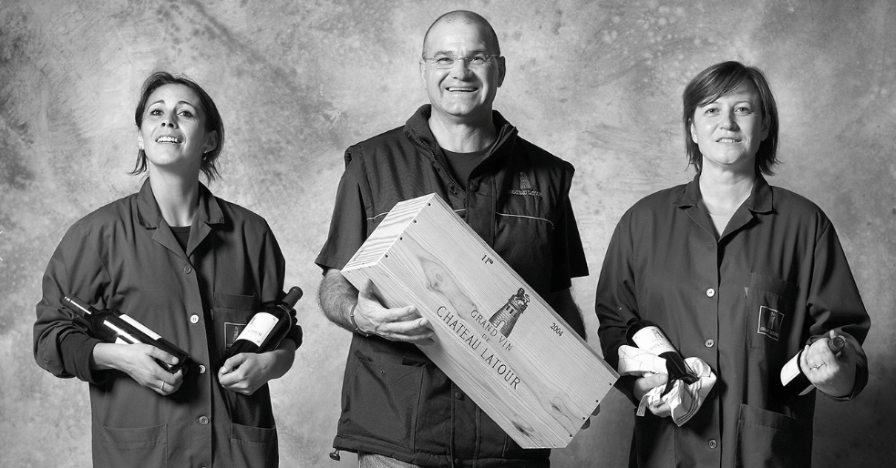 The team at Château Latour holding bottles and a wooden case of the Grand Vin, representing their craftsmanship and dedication.