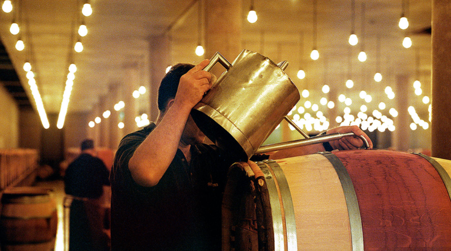 A winemaker at Château Latour pouring wine into barrels during the aging process in the cellar.