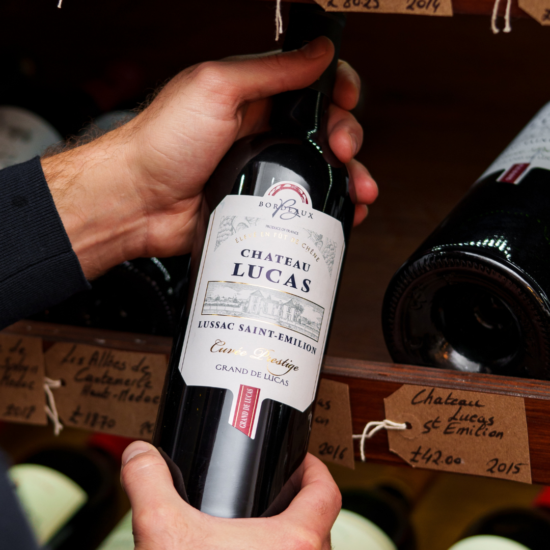 Person holding a bottle of Château Lucas Lussac Saint-Émilion, showcasing the wine in a retail setting among other Bordeaux wines, highlighting the Cuvée Prestige from the renowned Lussac Saint-Émilion appellation