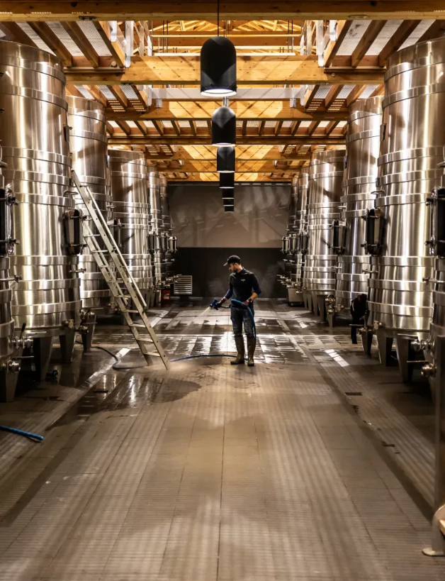 Inside Château Palmer's modern winery, featuring stainless steel fermentation tanks and a winemaker at work.