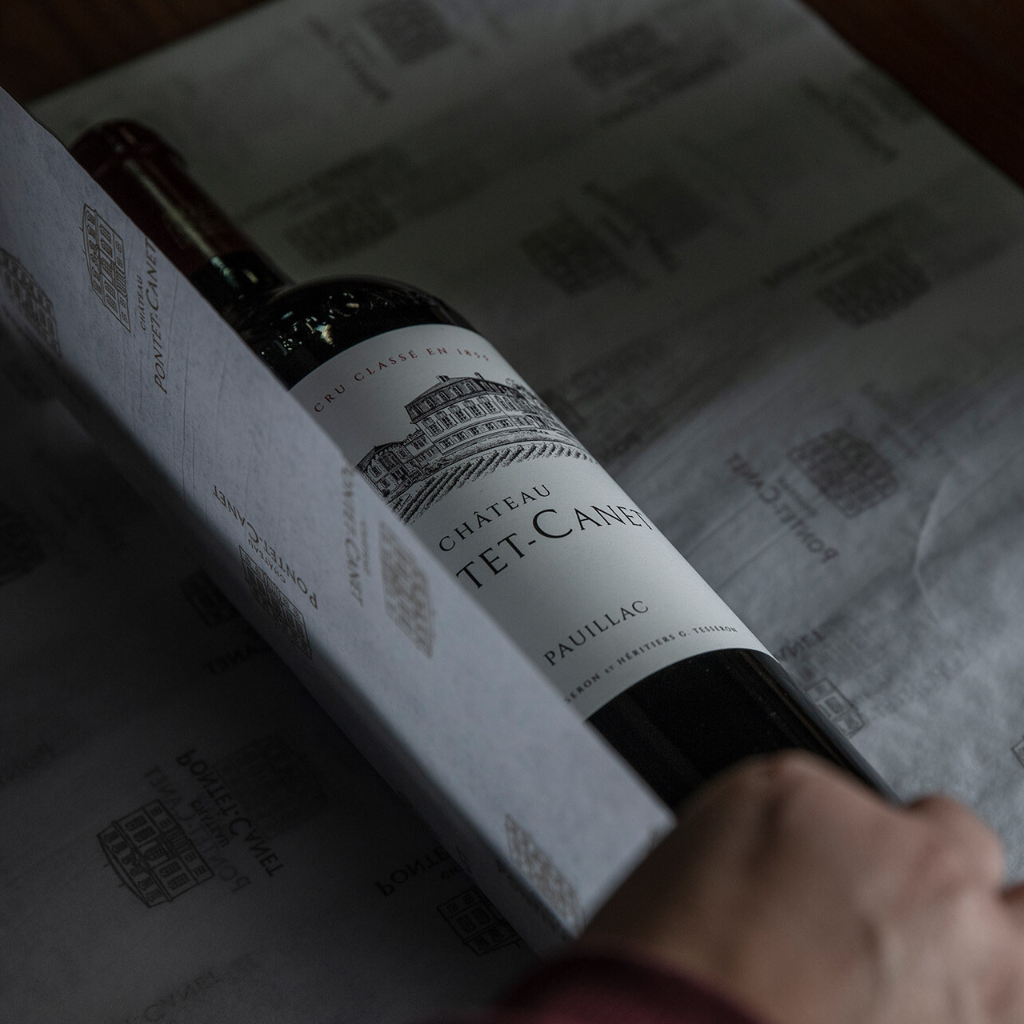 A bottle of Château Pontet-Canet Pauillac being carefully wrapped in branded packaging.