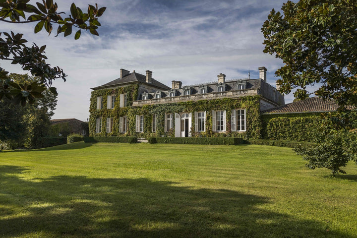 Exterior view of Château Talbot surrounded by lush greenery under a clear sky.