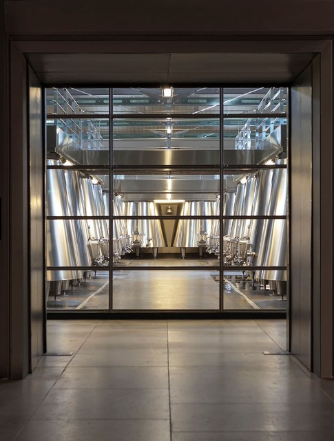 A sleek and modern winemaking facility at Cos d'Estournel, featuring stainless steel fermentation tanks behind glass walls.