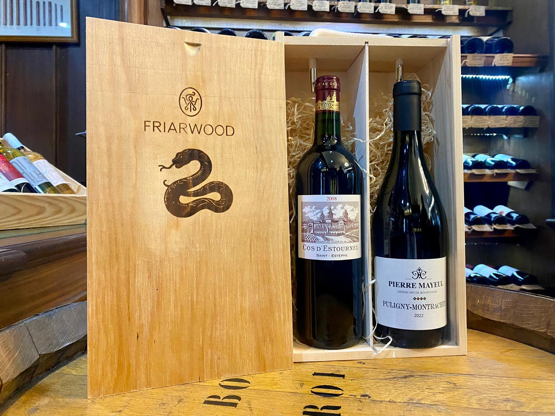 Custom-engraved wooden gift box featuring a snake symbol, containing 2008 Cos d'Estournel and 2022 Pierre Mayeul Puligny-Montrachet wines displayed on a wooden table in a wine shop.