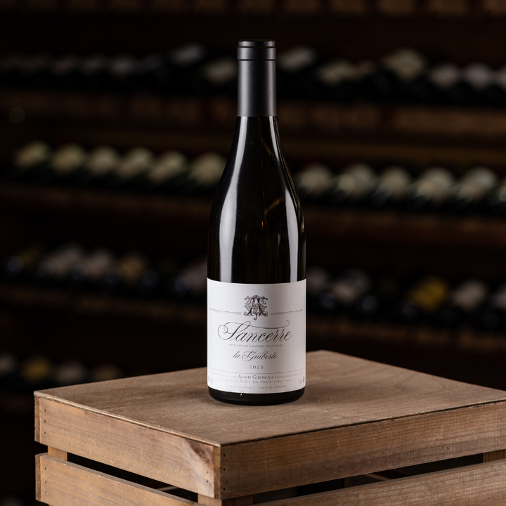 A bottle of Domaine Alain Gueneau Sancerre La Guiberte, a French Sauvignon Blanc wine, resting on a wooden crate in front of a wine cellar.