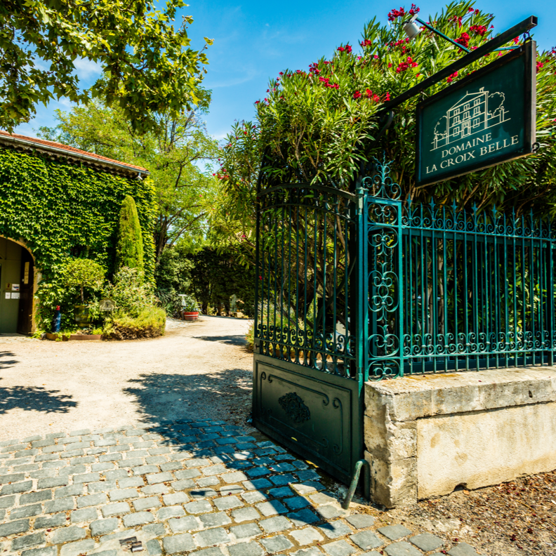 Entrance to Domaine La Croix Belle winery in the Languedoc region, surrounded by lush greenery and iron gates.