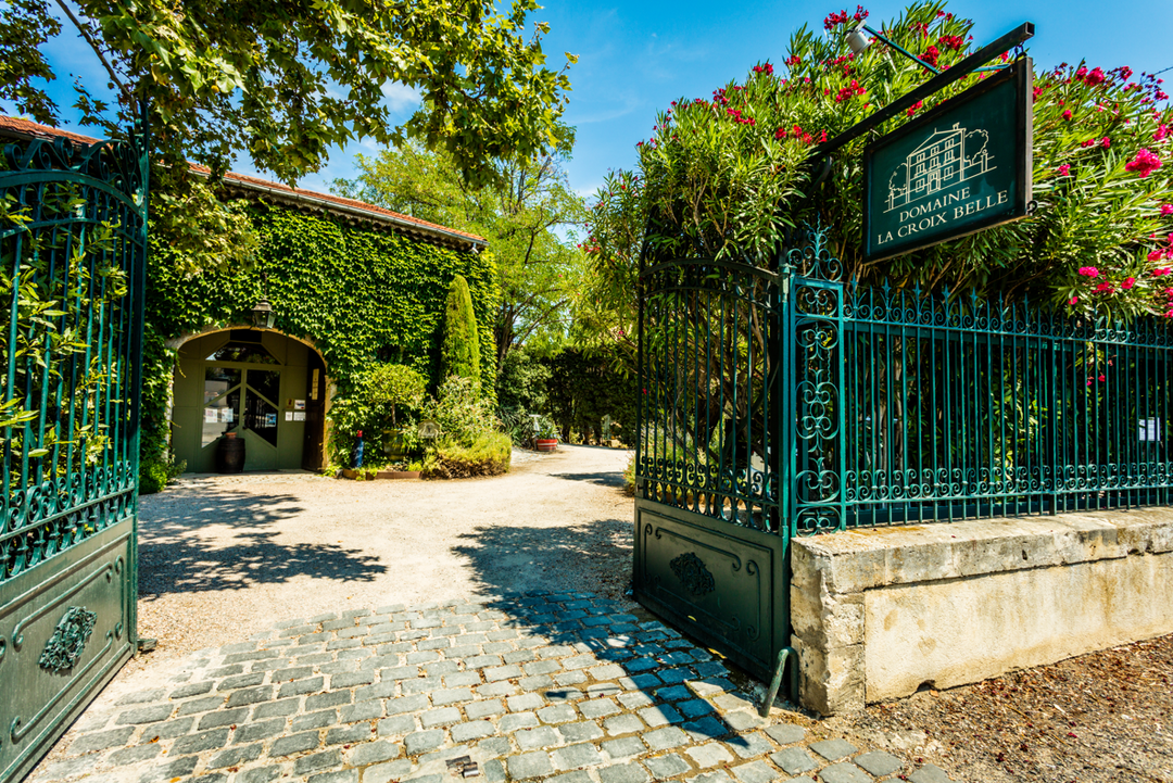 Entrance to Domaine La Croix Belle winery in the Languedoc region, surrounded by lush greenery and iron gates.