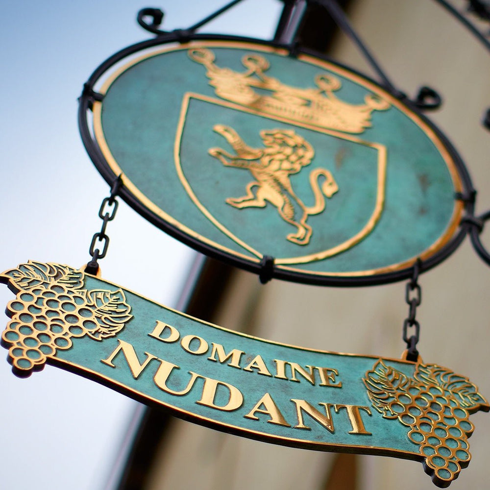 Ornate sign of Domaine Nudant in Burgundy, featuring a crest with a lion and grape cluster, representing the historic French winery known for its quality wines