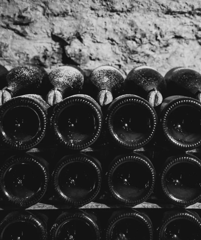 A stack of dusty, aging wine bottles in a dimly lit cellar, highlighting the art of fine wine maturation.