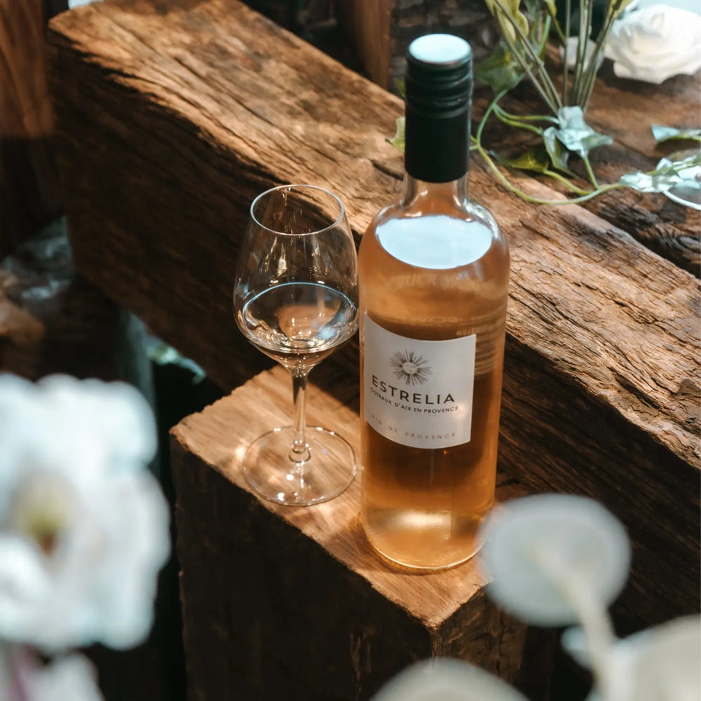 A bottle of Estrelia Rosé wine placed on rustic wood with a glass, surrounded by elegant floral arrangements.