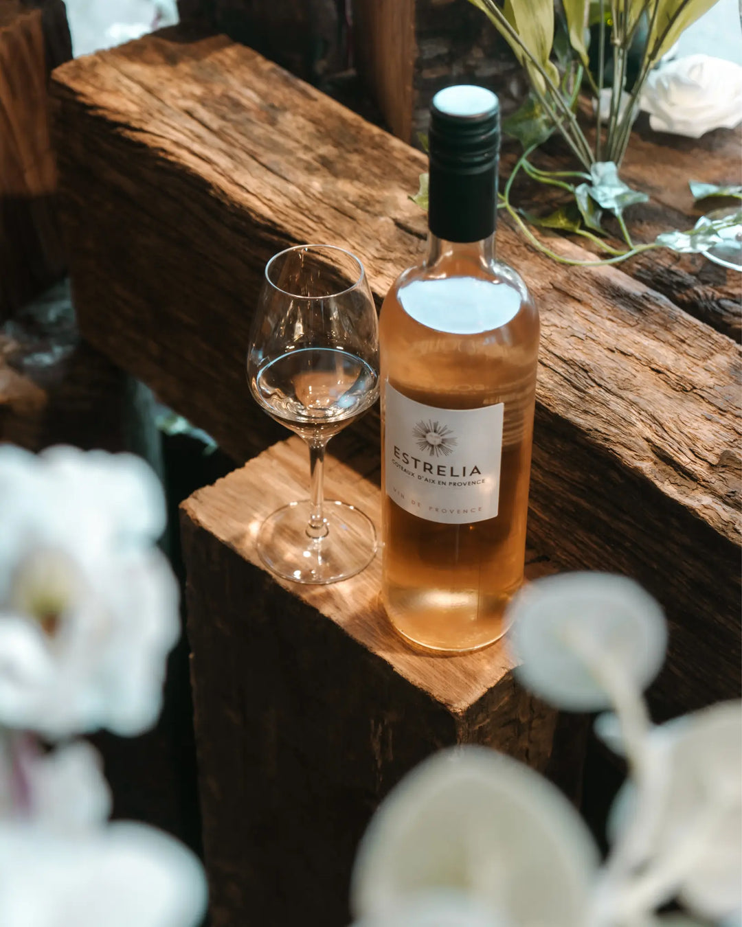 A bottle of Estrelia Rosé wine placed on rustic wood with a glass, surrounded by elegant floral arrangements.