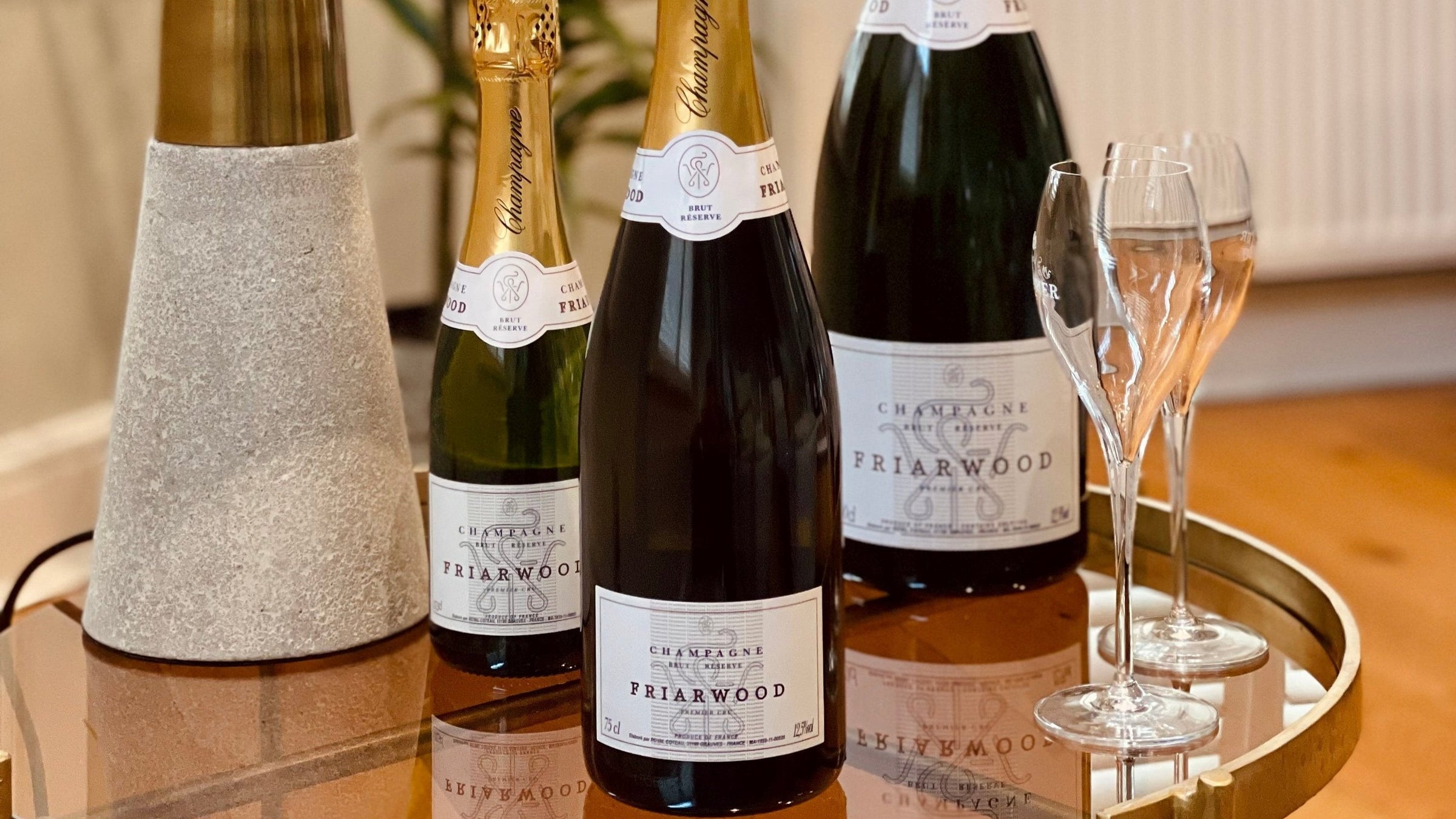 Three bottles of Friarwood Champagne Brut Reserve displayed elegantly with champagne flutes on a polished surface, showcasing the premium sparkling wine from Friarwood Wines & Spirits.