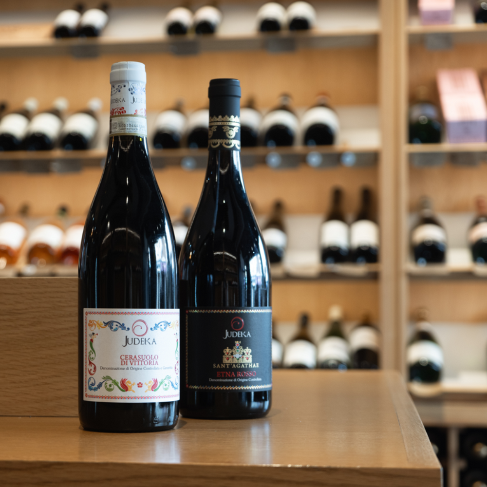 A display of Judeka wines in a shop, featuring two bottles: Judeka Cerasuolo di Vittoria and Judeka Etna Rosso.
