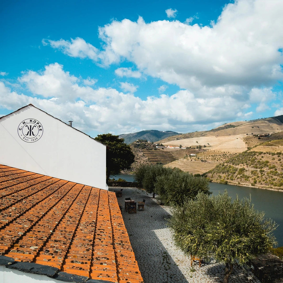 Kopke winery building near the Douro River, featuring a tiled roof and a scenic background of vineyards and hills.