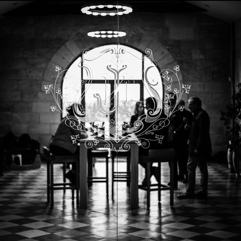 Black and white image of La Conseillante winery entrance, showcasing the etched glass emblem and a glimpse of visitors inside, reflecting elegance and tradition.