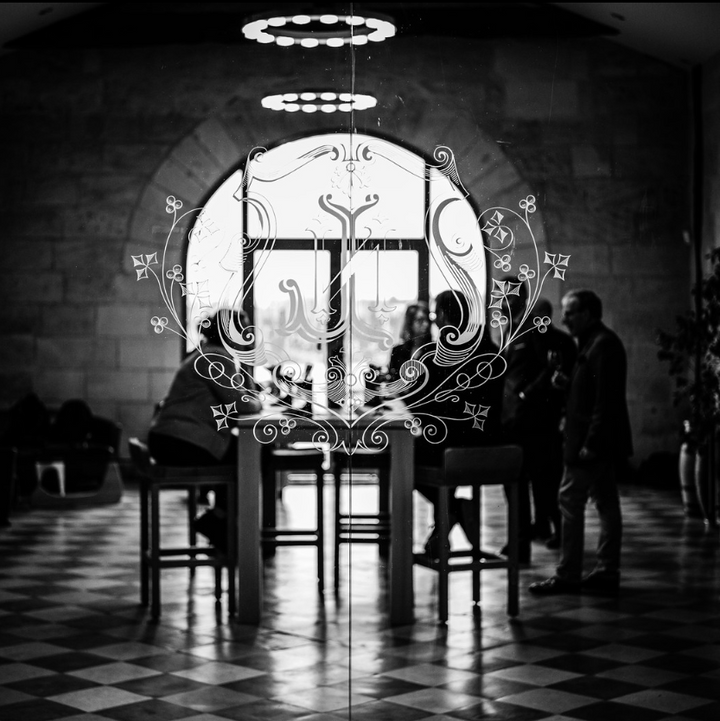 Black and white image of La Conseillante winery entrance, showcasing the etched glass emblem and a glimpse of visitors inside, reflecting elegance and tradition.