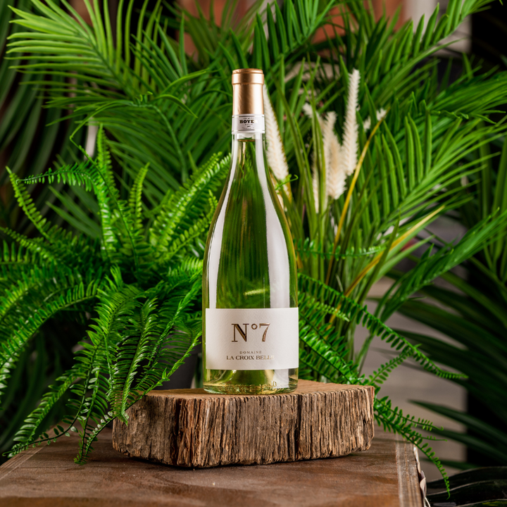  A bottle of La Croix Belle No. 7 Rose wine on a wooden slice, surrounded by lush greenery.