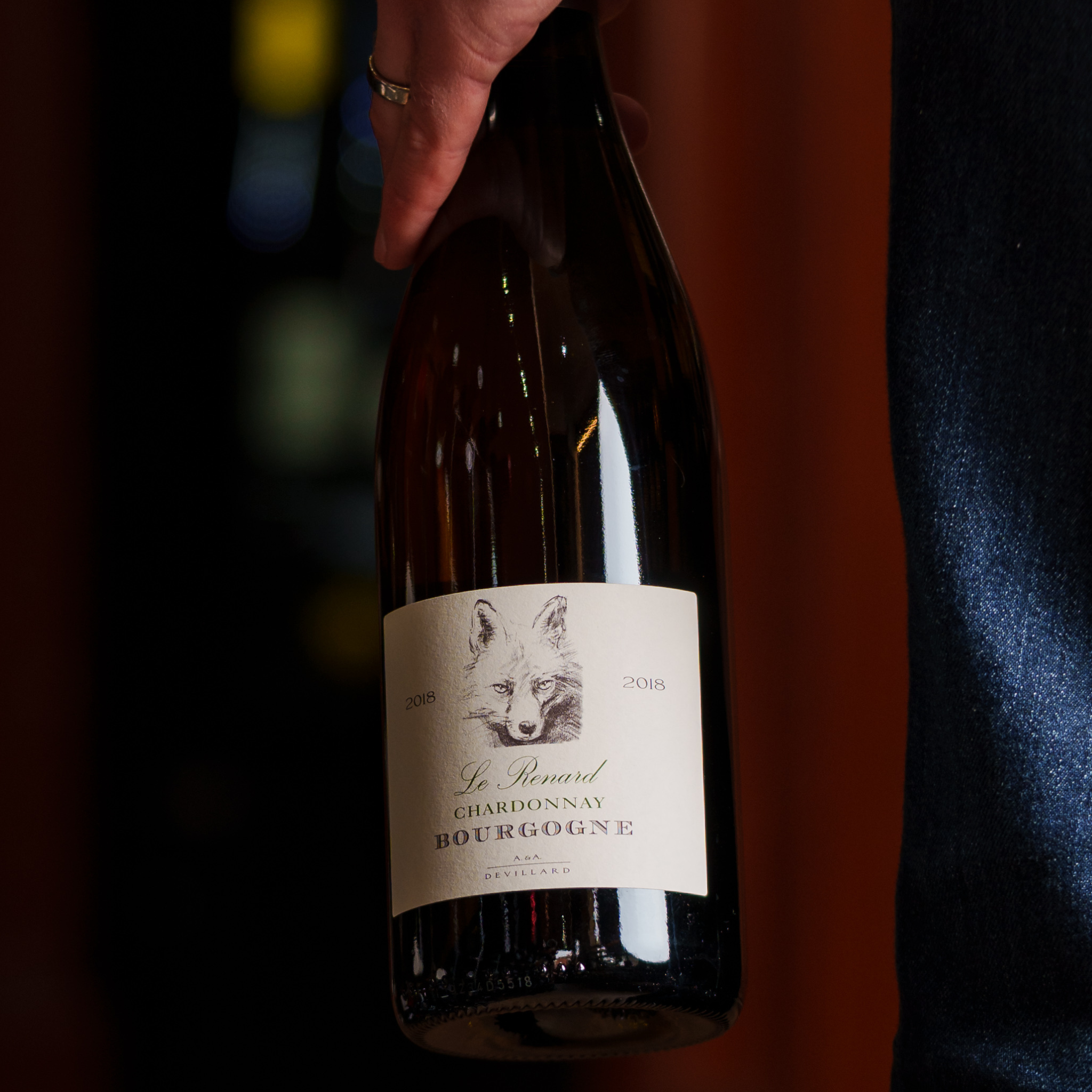 A person holding a bottle of Le Renard Chardonnay 2018 from Bourgogne, a refined Burgundy white wine with elegant citrus notes and subtle oak influence.