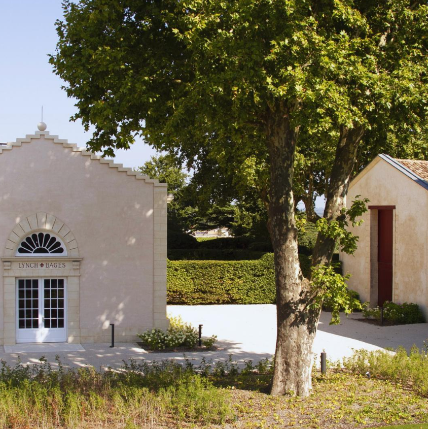 The exterior view of the Lynch Bages estate surrounded by greenery on a sunny day.