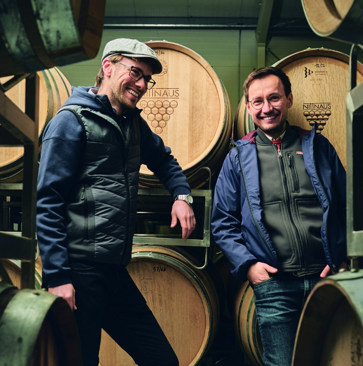 The winemakers at Gebrüder Nittnaus standing by wooden barrels in their wine cellar, showcasing the craftsmanship of Austrian winemaking.