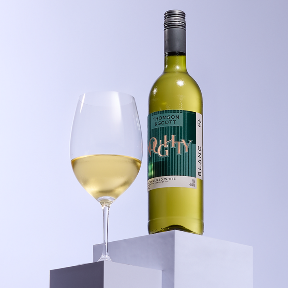 Noughty Blanc non-alcoholic white wine bottle by Thomson & Scott paired with a glass of white wine.