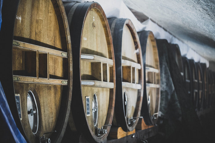 A row of oak wine barrels in a dimly lit cellar, showcasing traditional aging methods for fine wines.