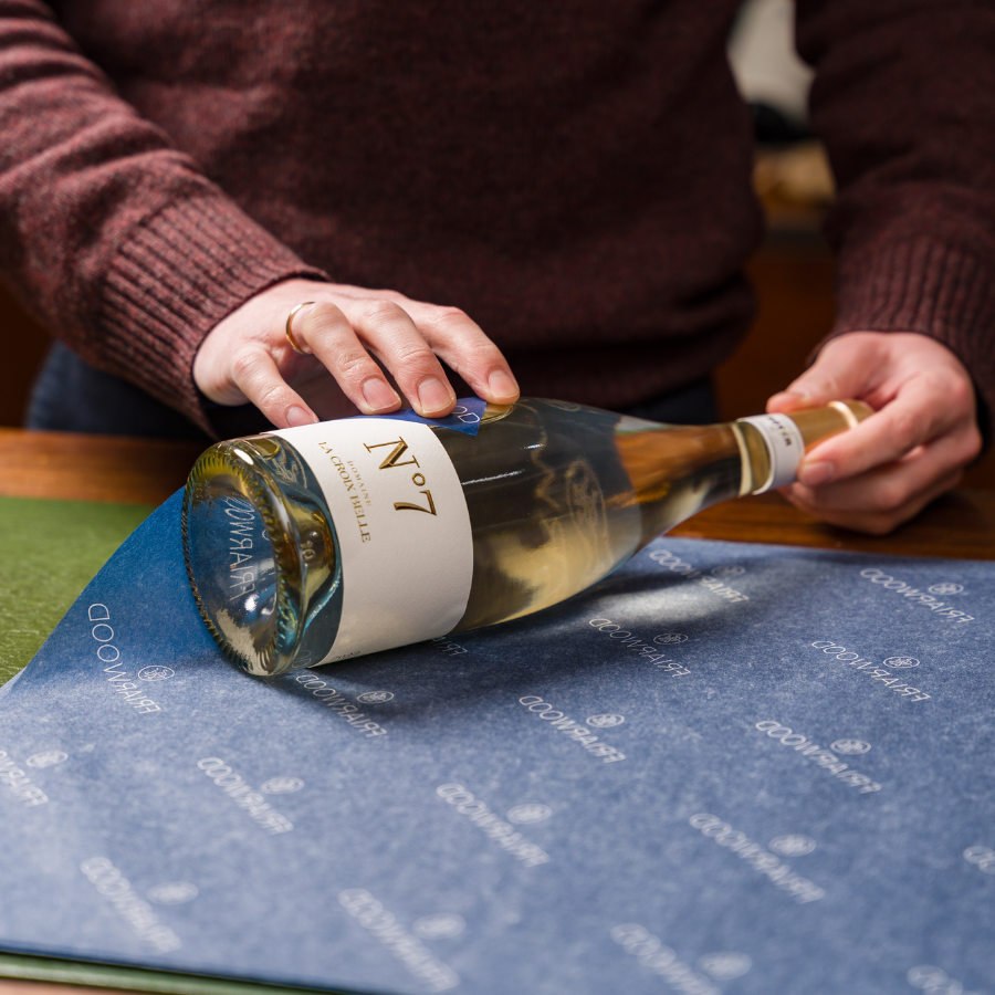 A person carefully wrapping a bottle of No. 7 white wine from La Croix Belle in branded wrapping paper, showcasing an elegant wine packaging process.