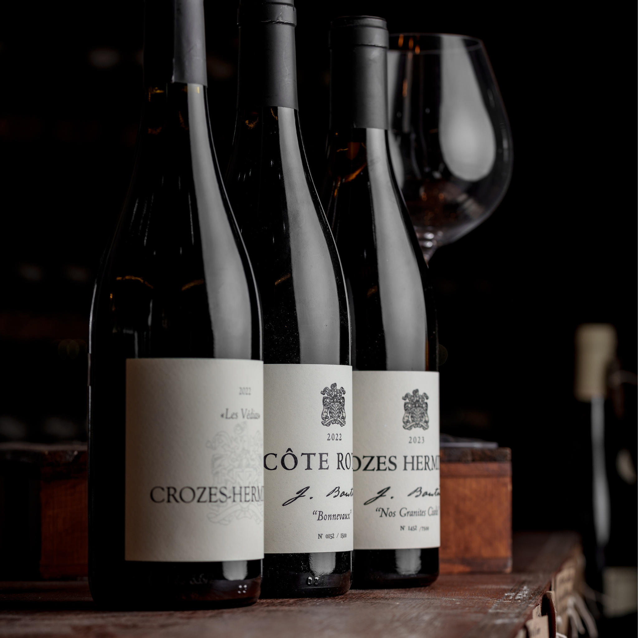 Three bottles of Rhône wines, including Crozes-Hermitage and Côte-Rôtie, displayed elegantly against a dark background with a wine glass, showcasing the craftsmanship and heritage of French winemaking