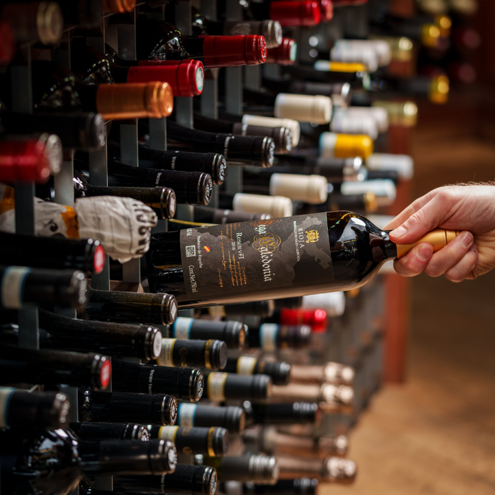 Hand picking a bottle of Rioja Reserva wine from a neatly arranged wine rack in a store, surrounded by various wine bottles showcasing a premium wine selection.