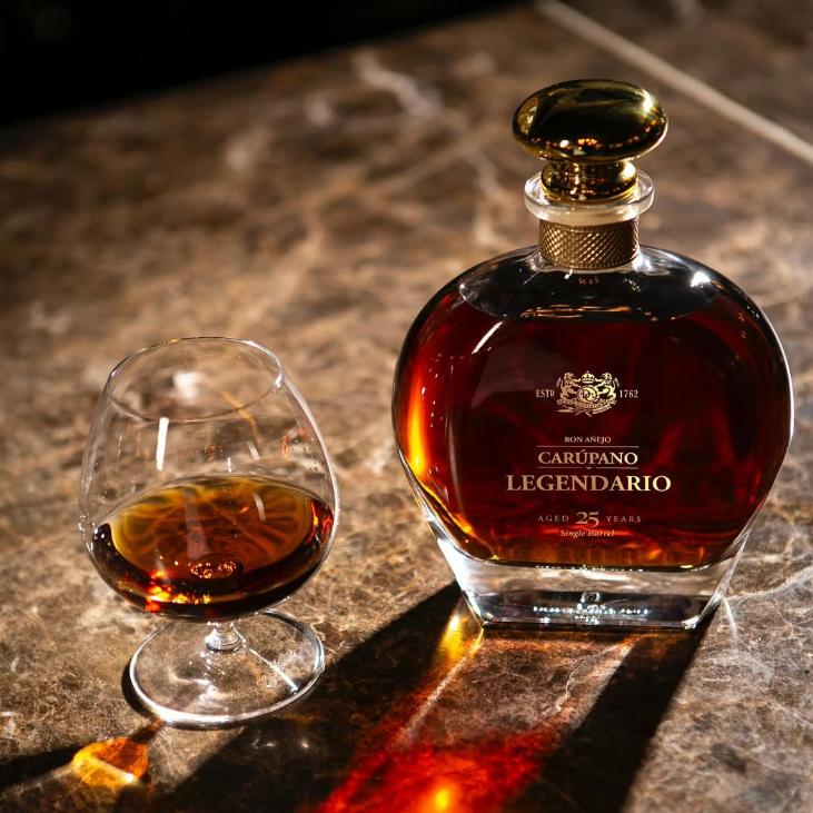 A bottle of Ron Carúpano Legendario 25-Year-Old rum on a marble surface, accompanied by a glass of poured rum.