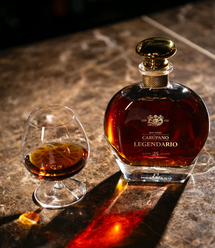 A bottle of Ron Carúpano Legendario 25-Year-Old rum on a marble surface, accompanied by a glass of poured rum.