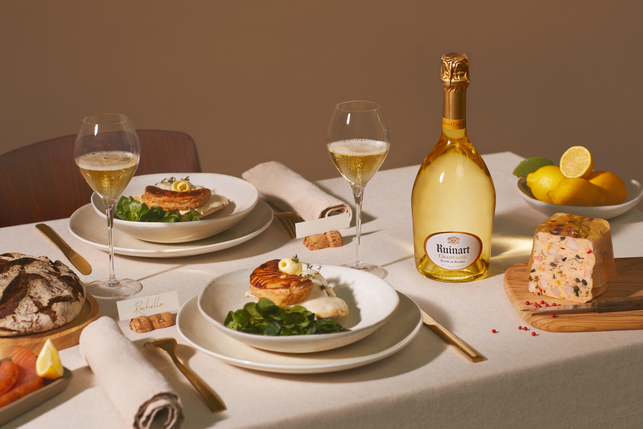 Ruinart Blanc de Blancs Champagne showcased on a luxurious dining table with elegant dishes, bread, and cheese, creating a perfect pairing experience.